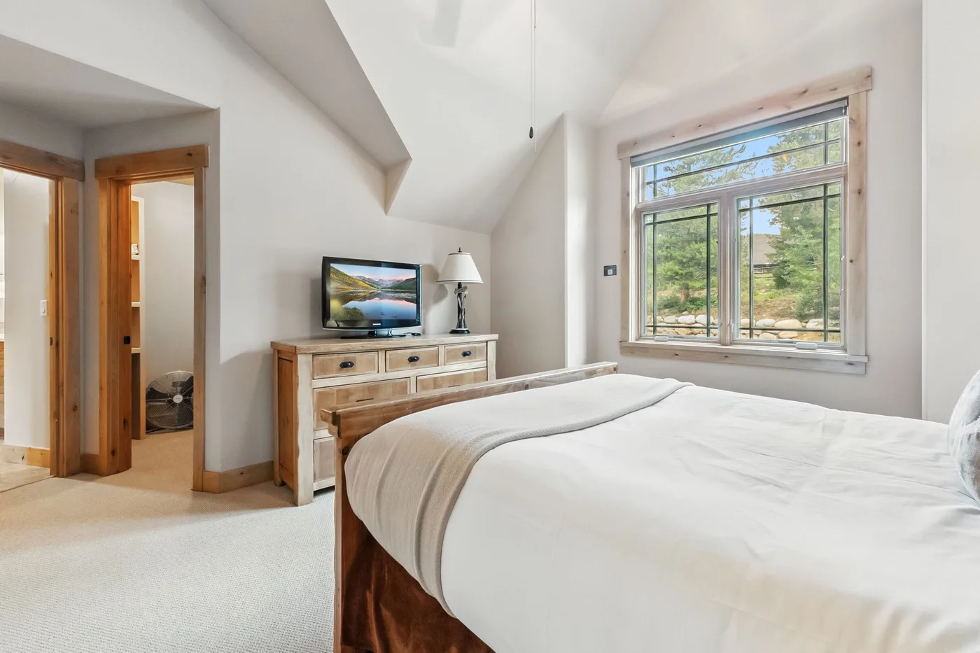 Un dormitorio luminoso con una cama tendida, una cómoda y una ventana grande.