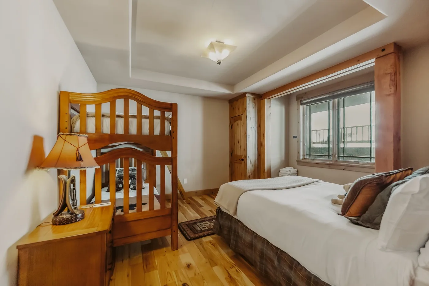Un dormitorio con una litera de madera y una cama más grande junto a una ventana.