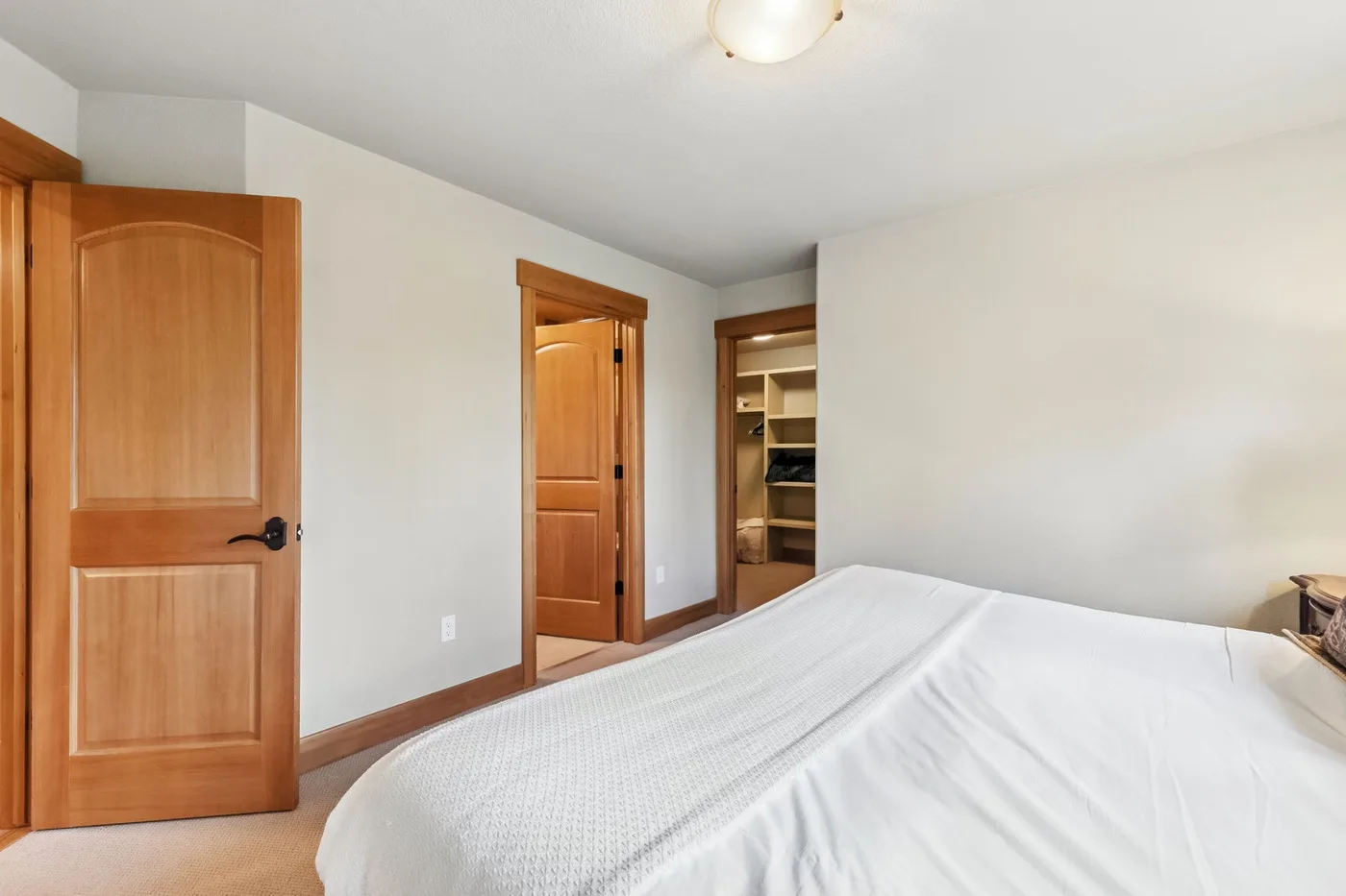 Un dormitorio con una cama bien tendida y puertas de madera abiertas.
