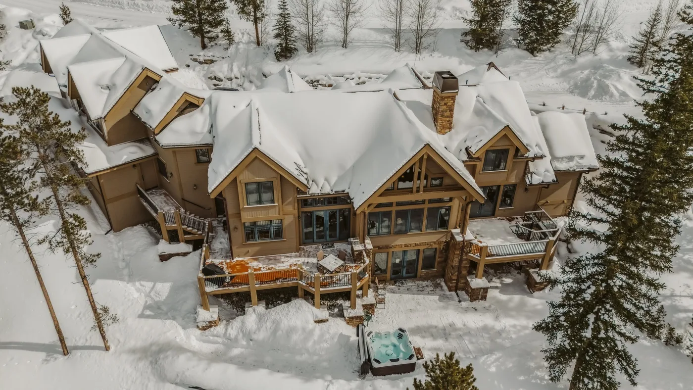 Un gran alojamiento con techos cubiertos de nieve y terrazas de madera está en un paisaje nevado.