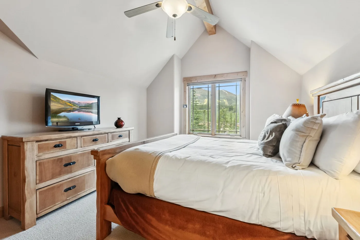 Un dormitorio con una cama, una cómoda de madera y ventanas con vistas a un paisaje verde.