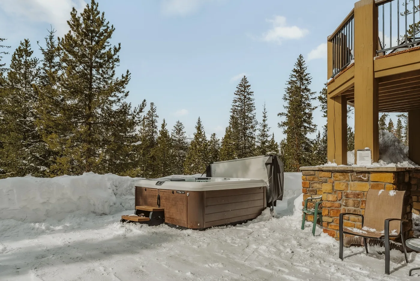 Una bañera de hidromasaje exterior está en un espacio nevado junto a una terraza de madera.