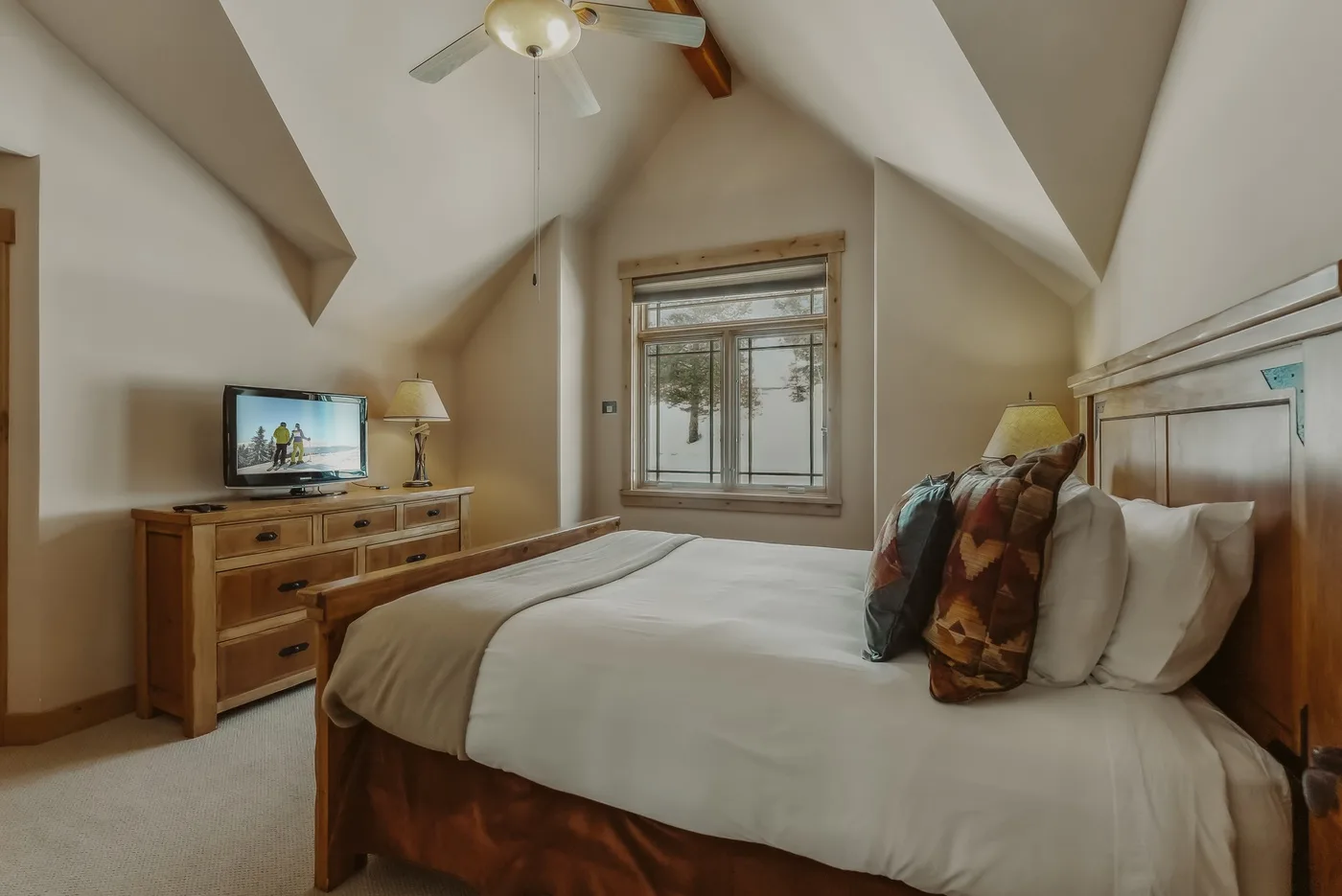 Un dormitorio con cama, cómoda de madera y ventana bajo un techo inclinado.
