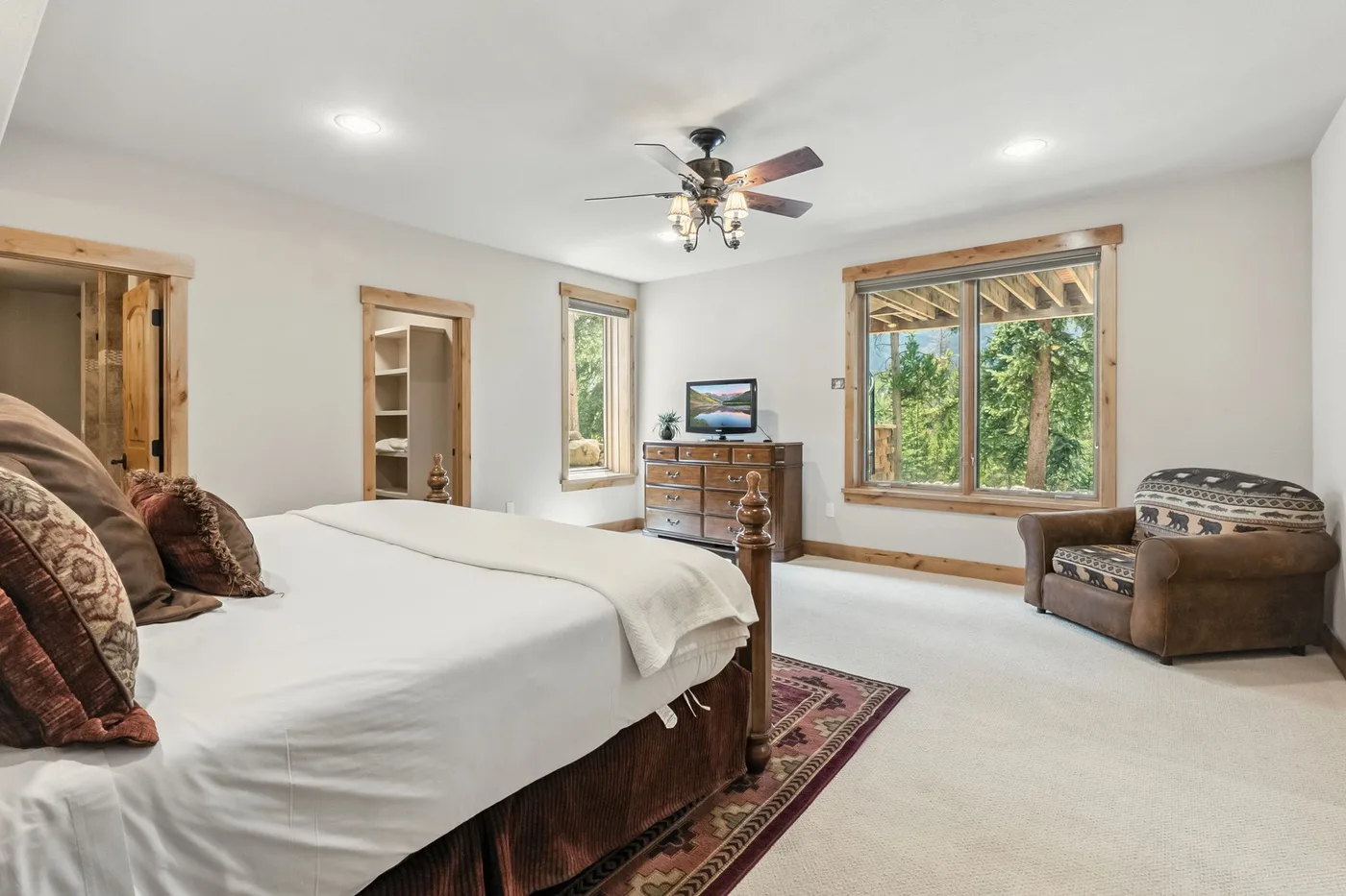 Un dormitorio con una cama grande, una cómoda de madera y ventanas con vistas a los árboles.