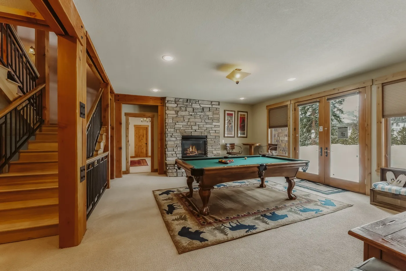 Una sala de juegos con mesa de billar, chimenea de piedra y ventanas grandes.