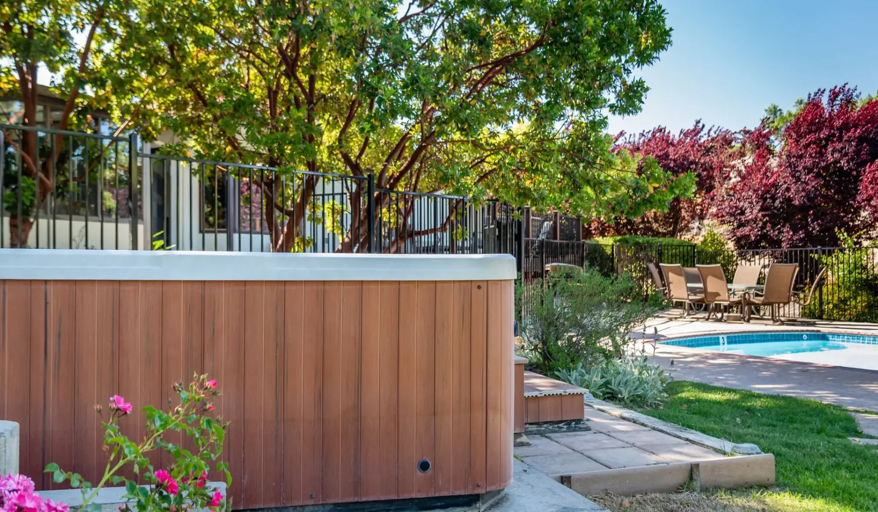 Una piscina exterior y una bañera de hidromasaje junto a un jardín.
