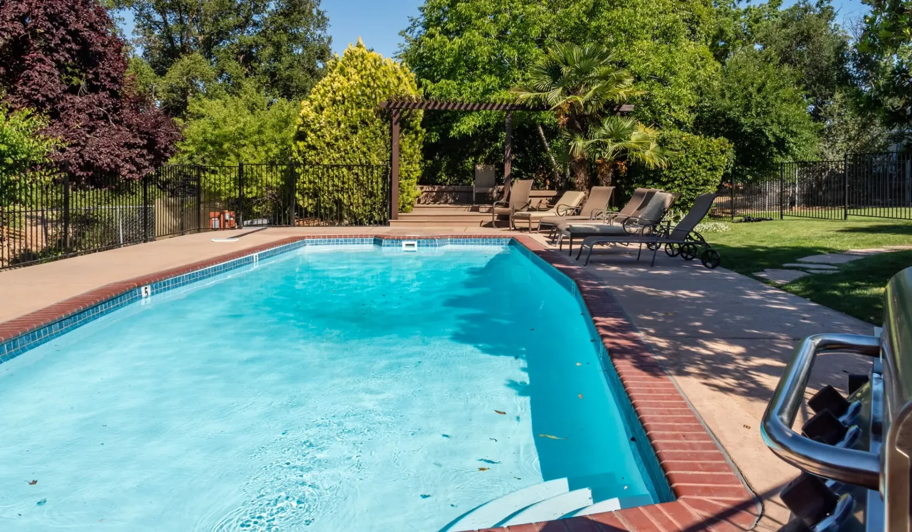 Una piscina al aire libre rodeada por una terraza pavimentada y asientos reclinables.