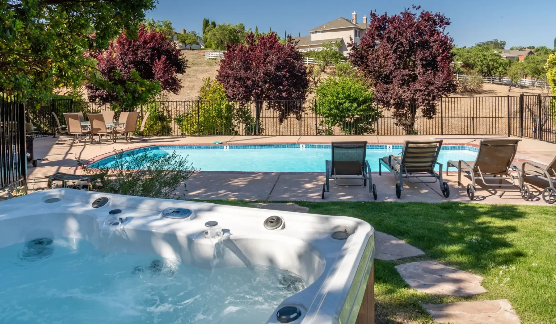 Una piscina al aire libre y un jacuzzi están rodeados de tumbonas y árboles.