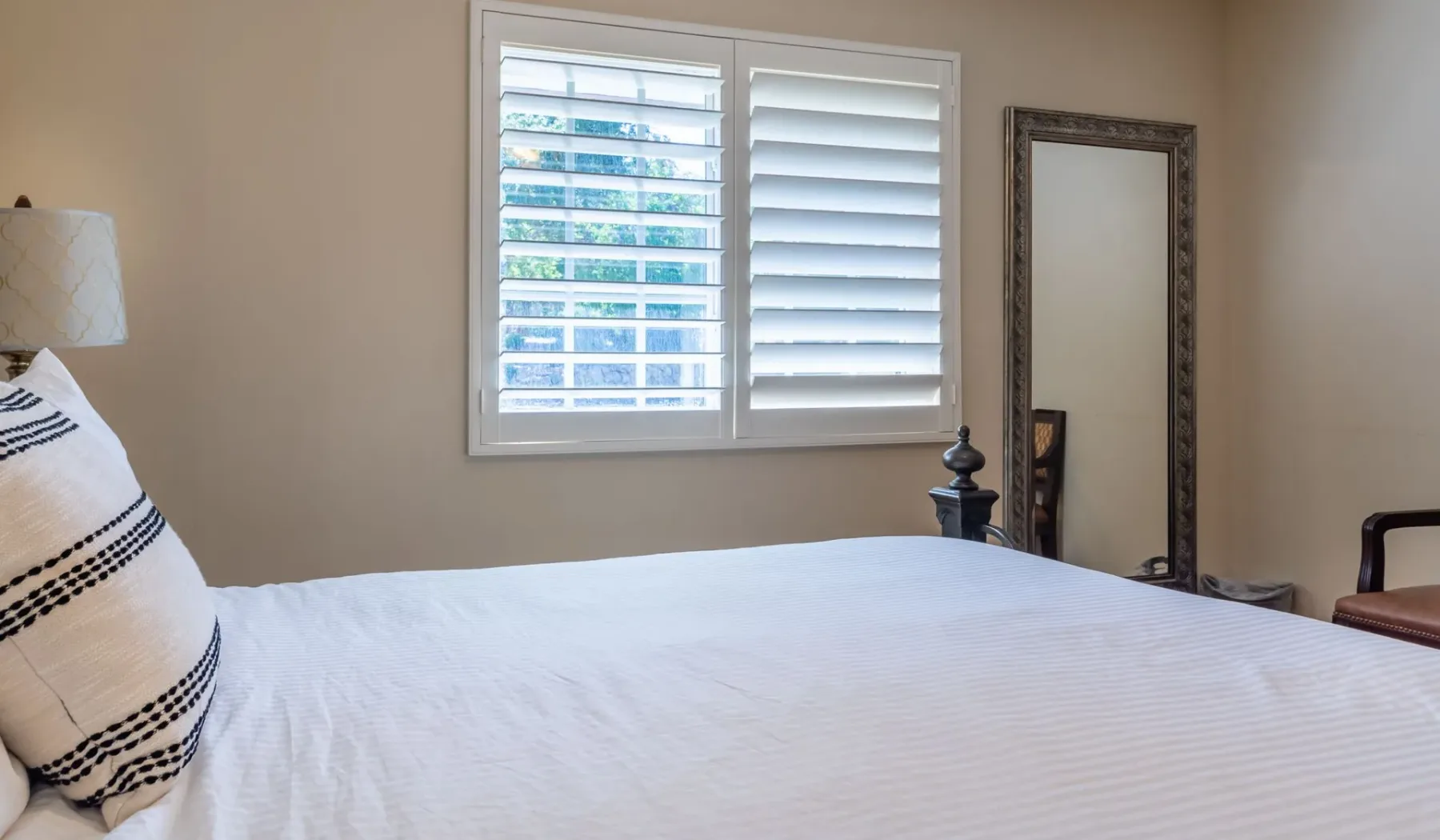 Un dormitorio con una cama bien tendida bajo una ventana con contraventanas blancas.