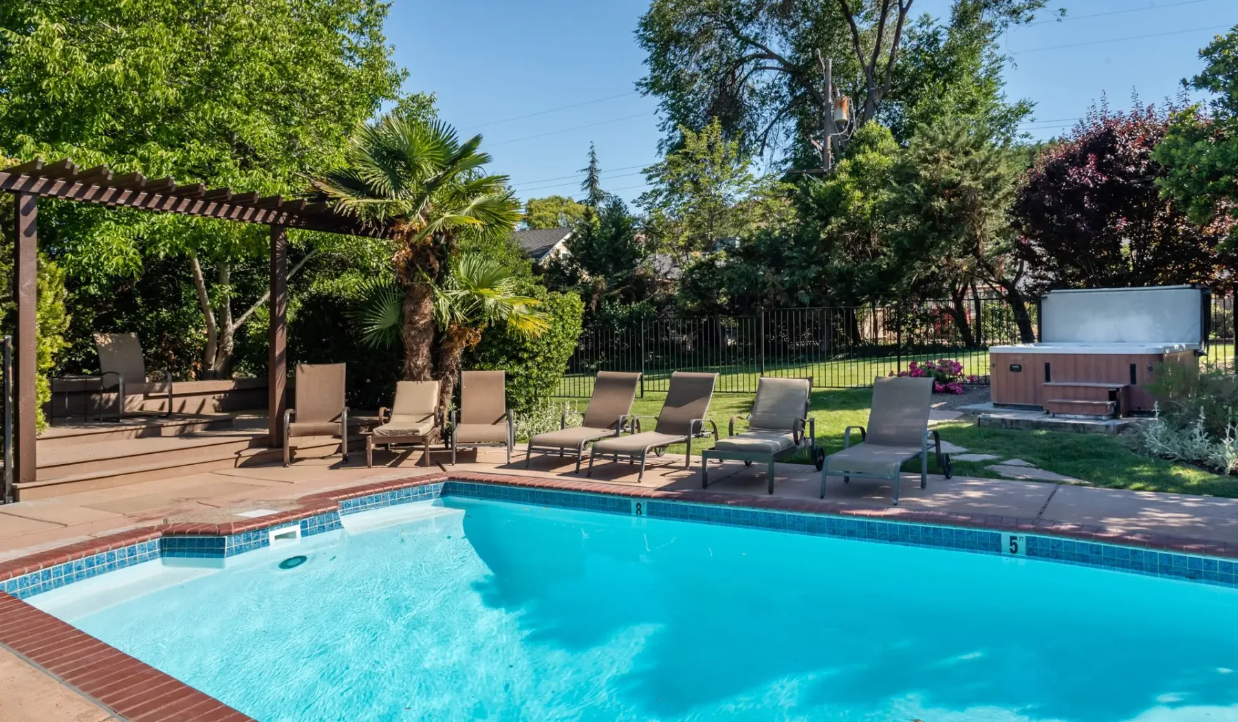 Una piscina en el patio está rodeada de asientos reclinables y árboles frondosos.