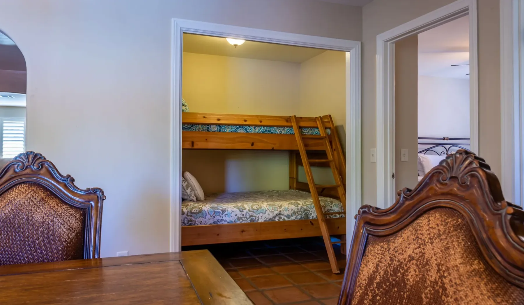 Una litera se ve en la entrada de un dormitorio junto a una mesa y sillas de madera.