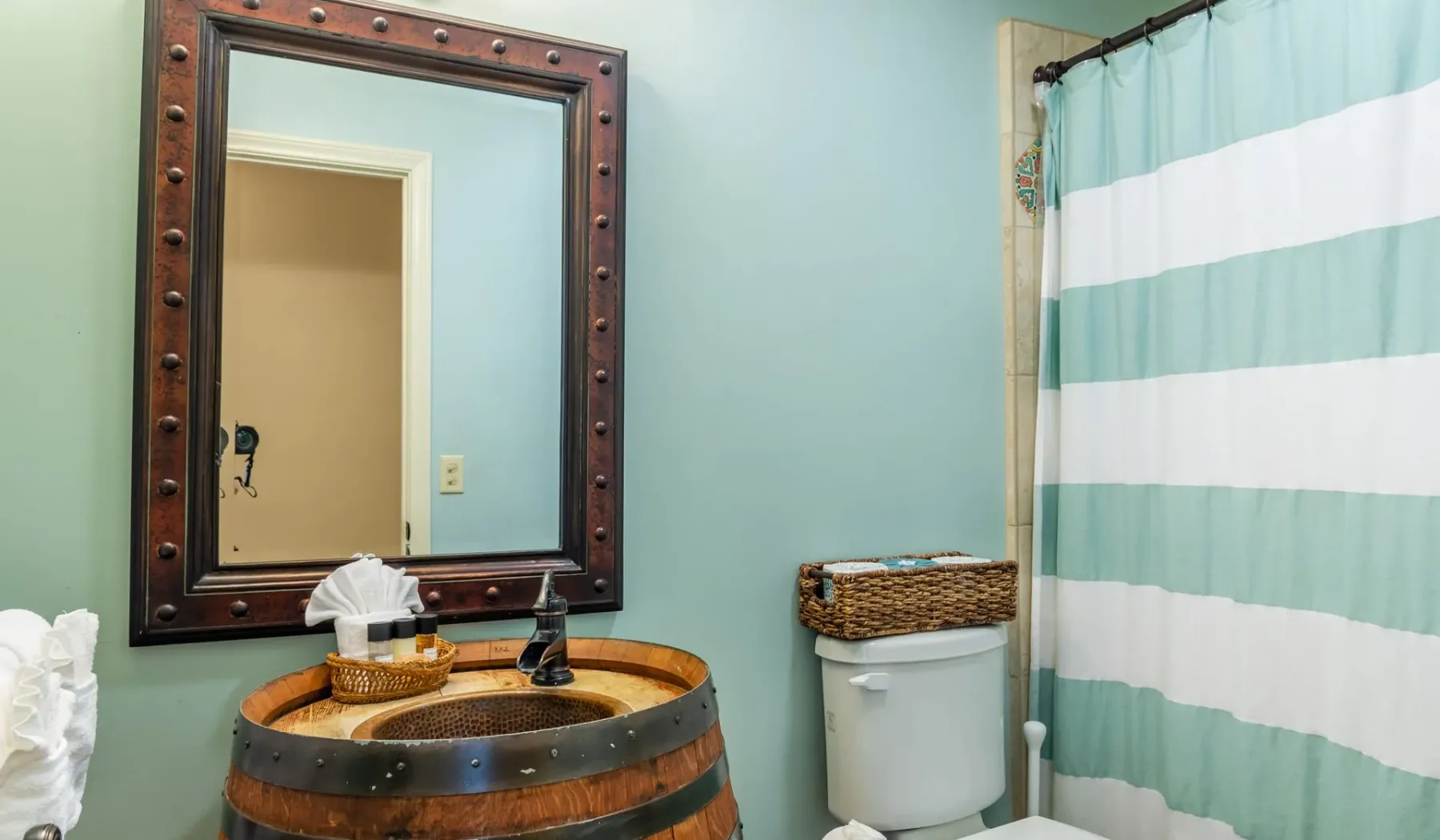 Un baño con un mueble de lavabo estilo barril, un espejo de pared y una cortina de ducha a rayas.