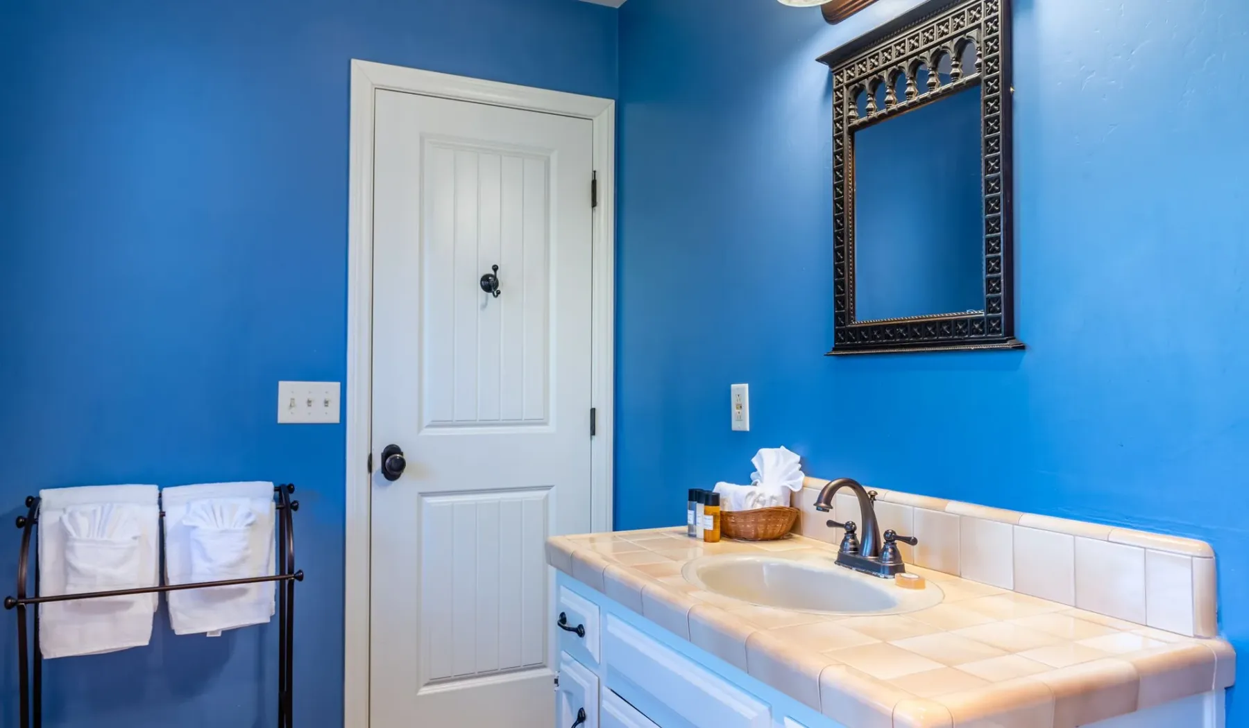 Un baño azul con lavabo sobre un tocador de azulejos y una puerta blanca.