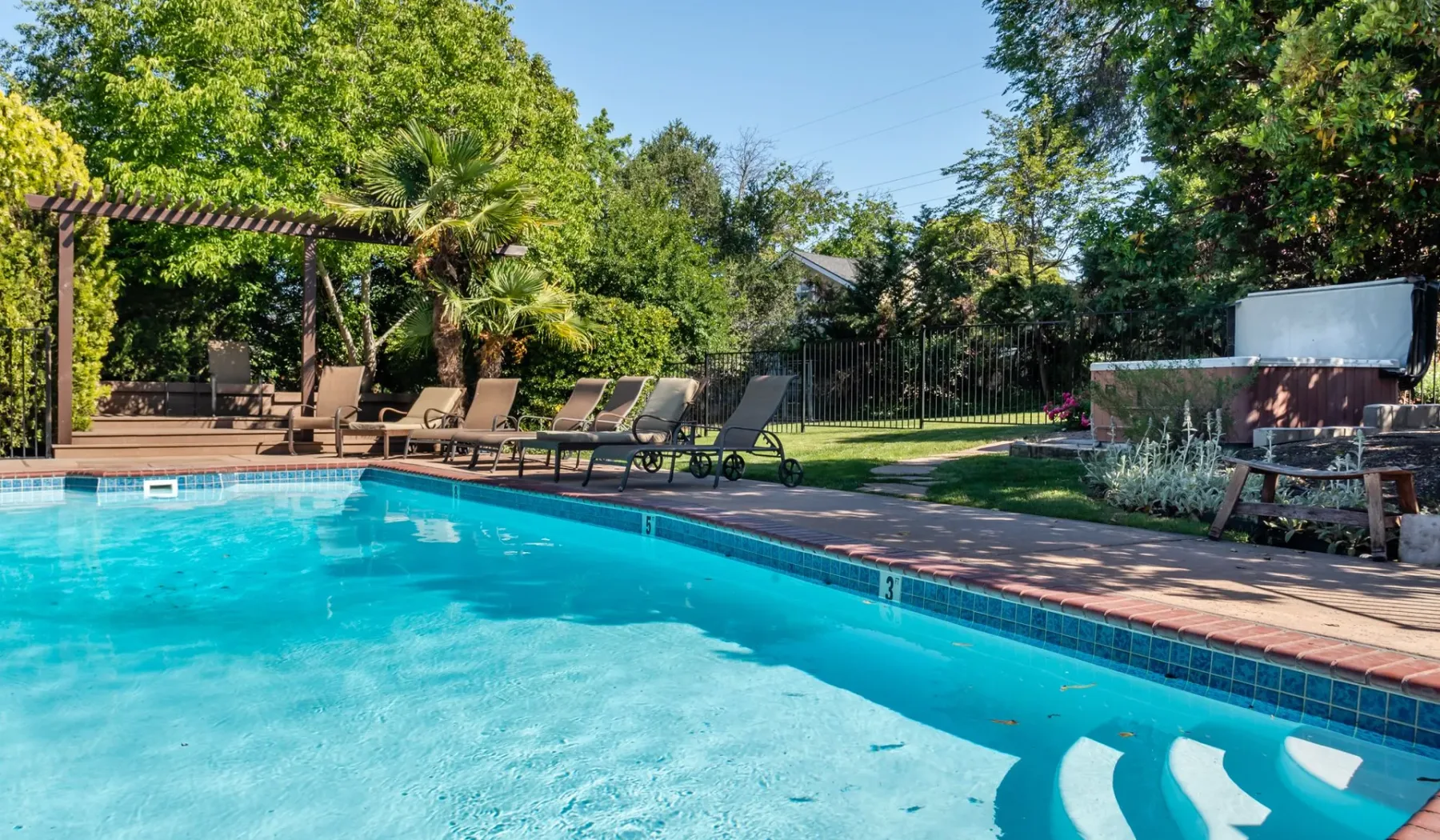 Una piscina al aire libre junto a asientos reclinables y vegetación frondosa.