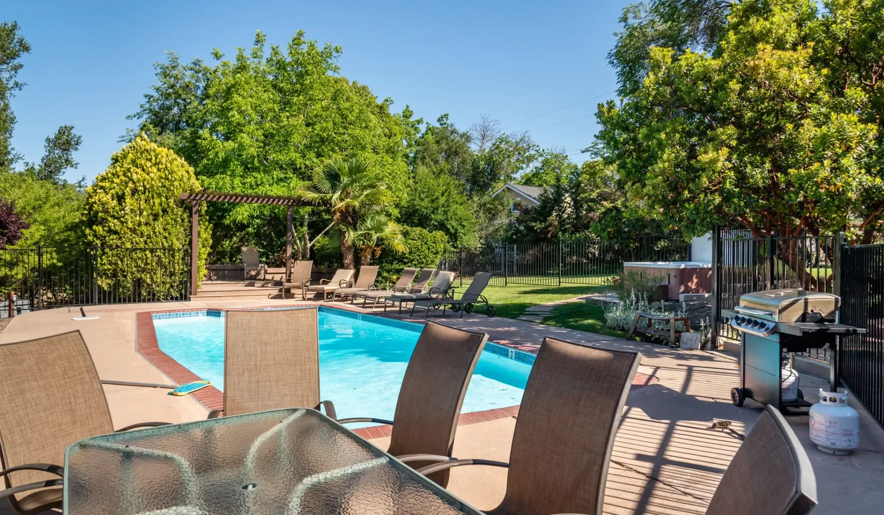 Una piscina al aire libre está rodeada de asientos reclinables y árboles frondosos.