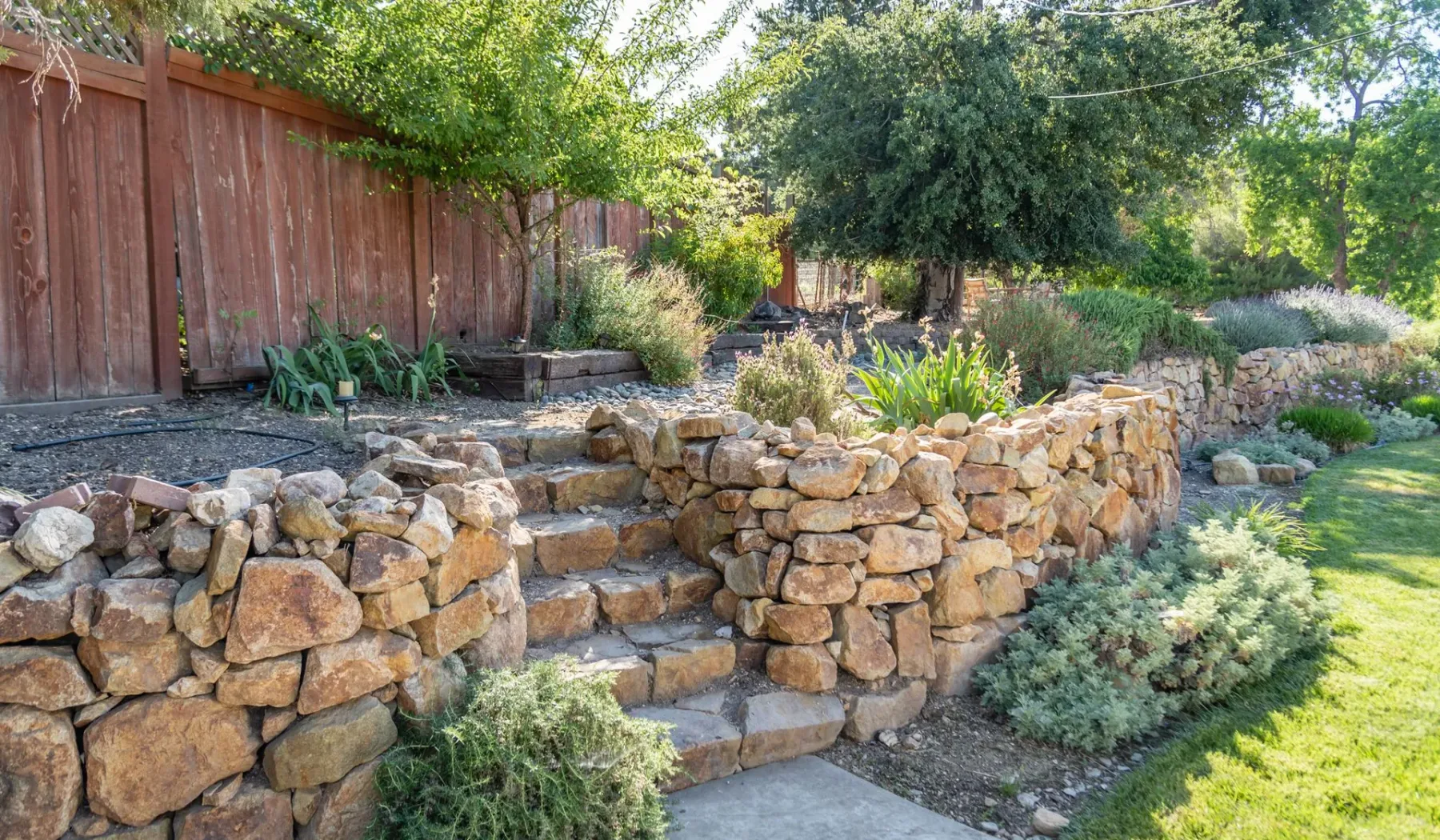 Un jardín ajardinado con muros de piedra y escalones.