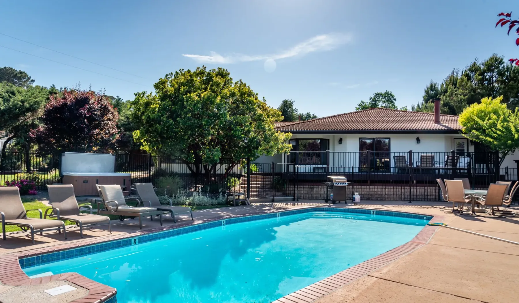 Una piscina al aire libre está junto a un patio con asientos y una casa al fondo.