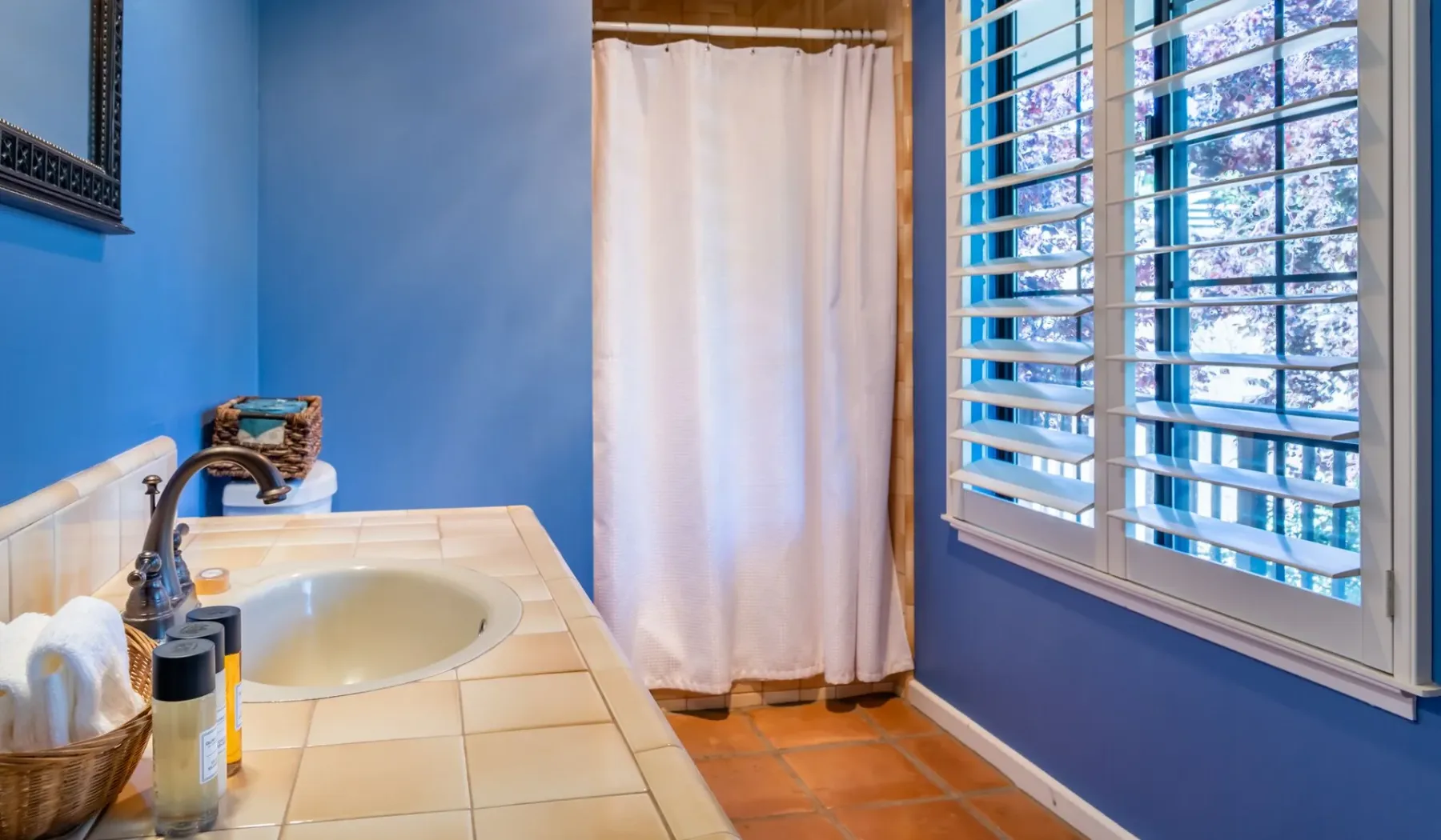 Un baño azul con lavabo sobre una encimera de azulejos y una ducha con cortina.