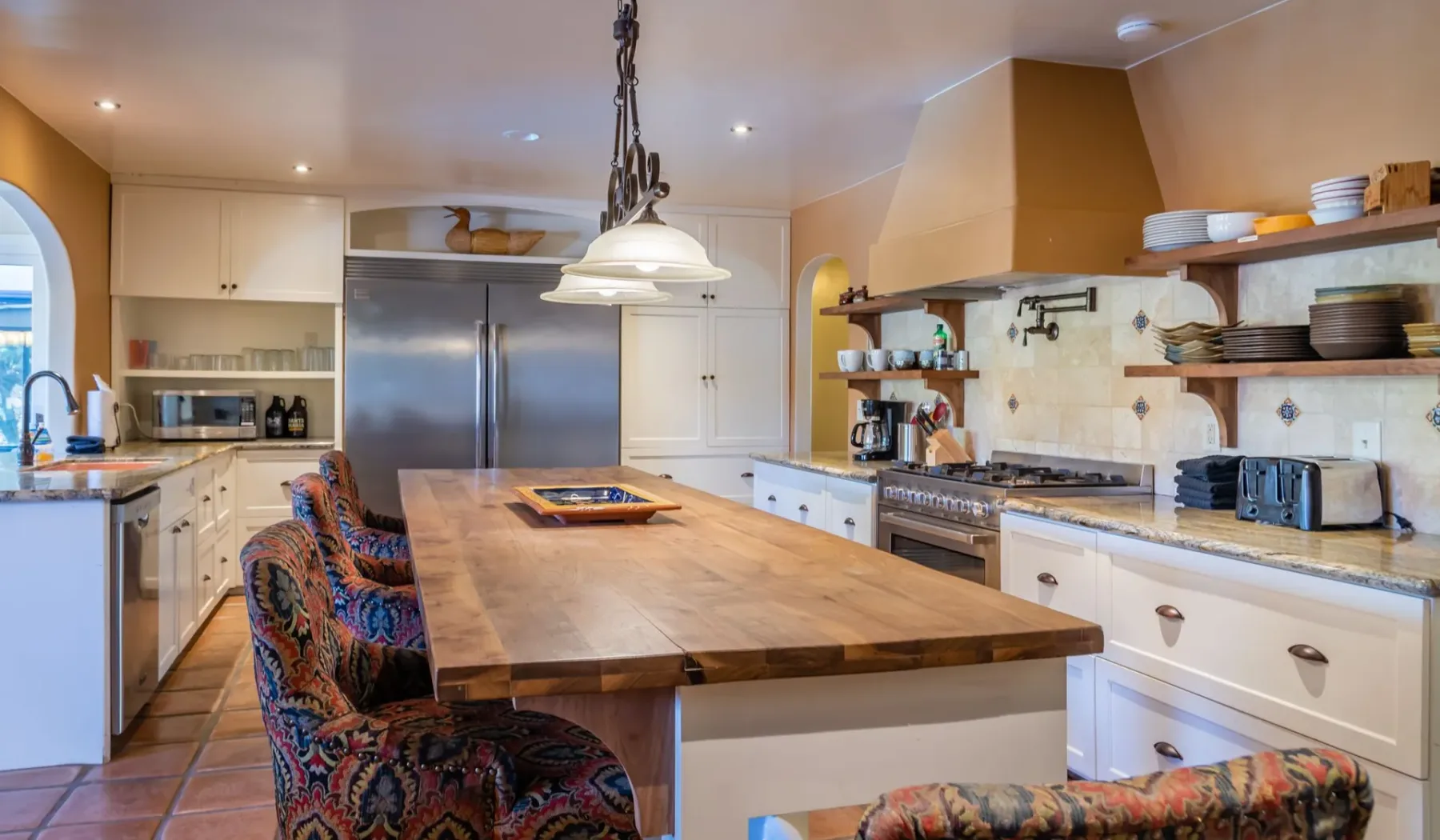 Una cocina amplia con una isla de madera y estantes abiertos en la pared.