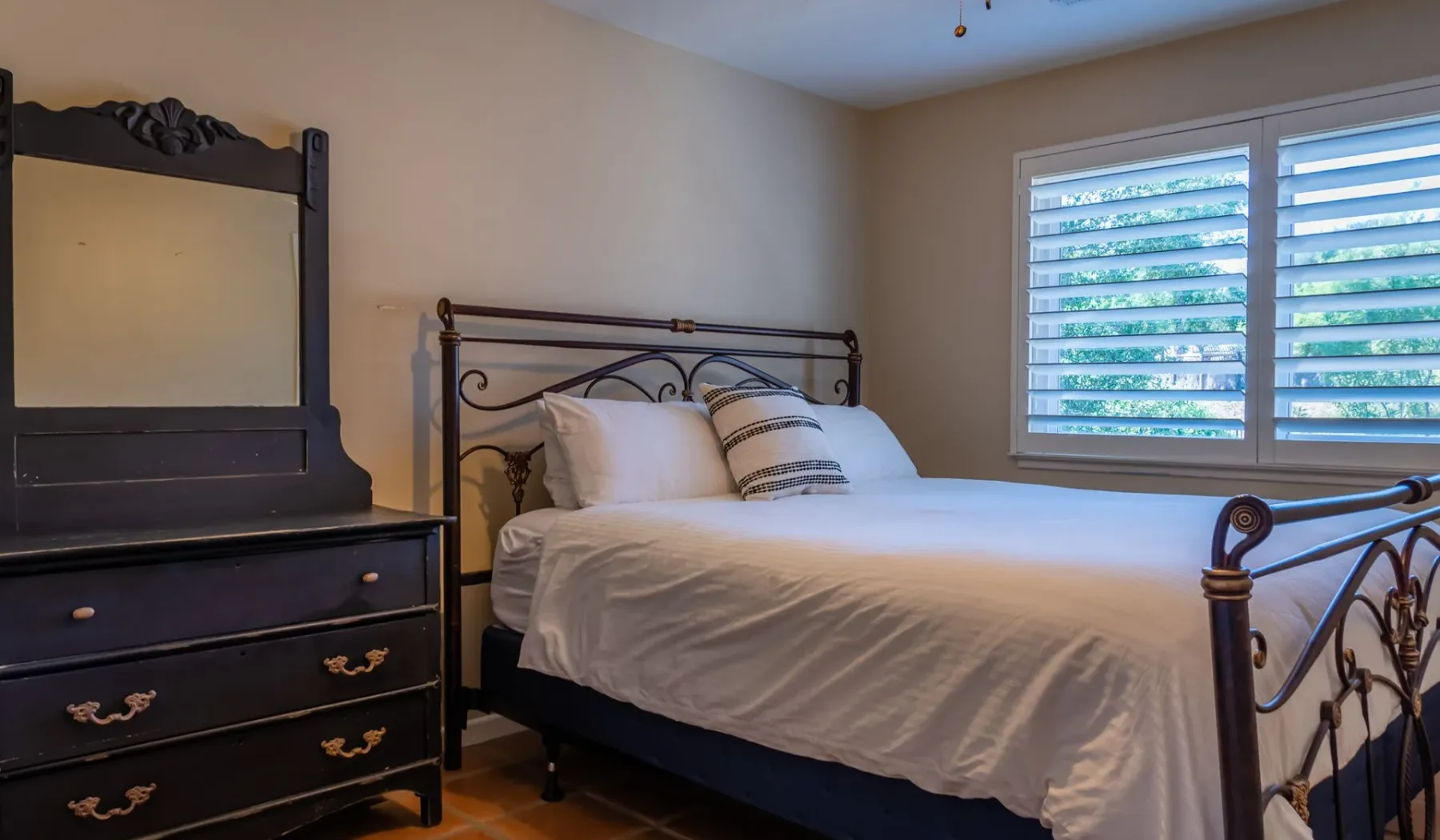 Un dormitorio con una cama de armazón metálico y una ventana con persianas horizontales.