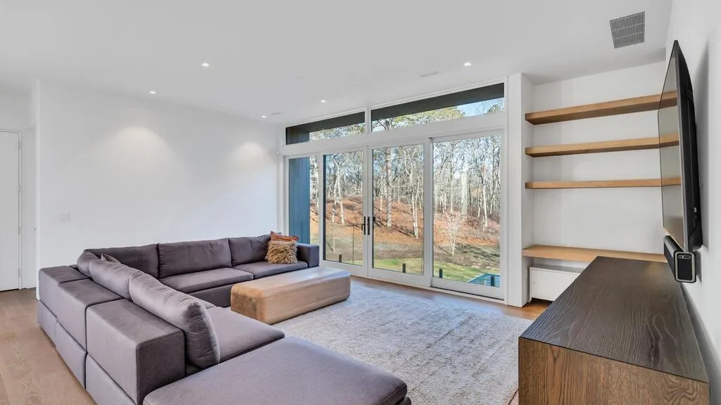 Una sala luminosa con un sofá seccional y grandes puertas de vidrio con vista a árboles.