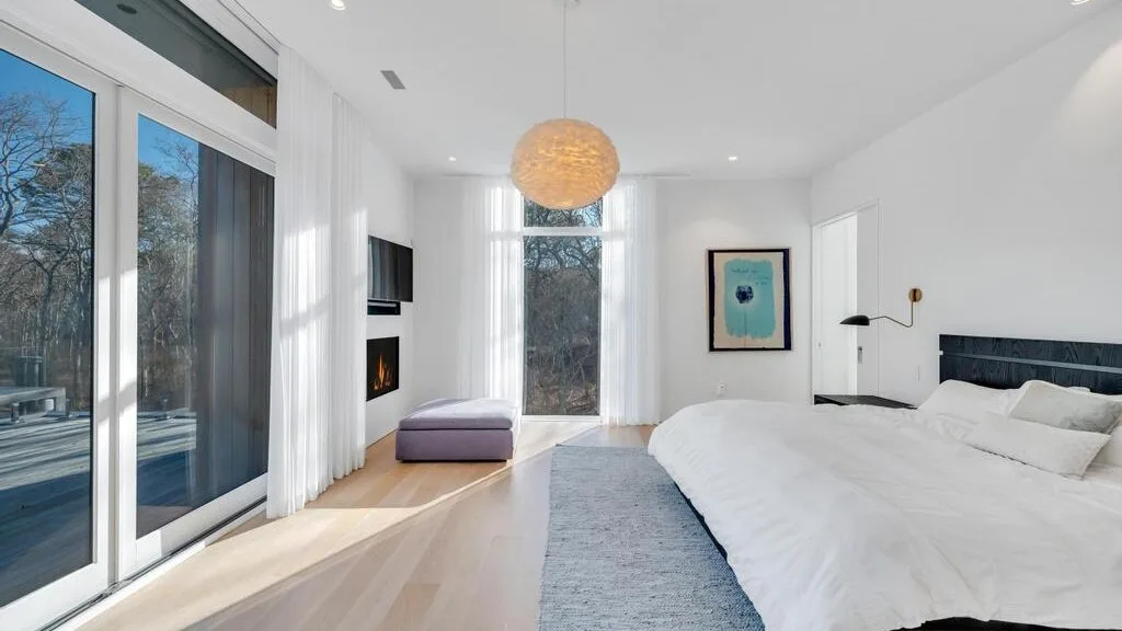 Un dormitorio luminoso con una cama grande, ventanas altas y una lámpara colgante.