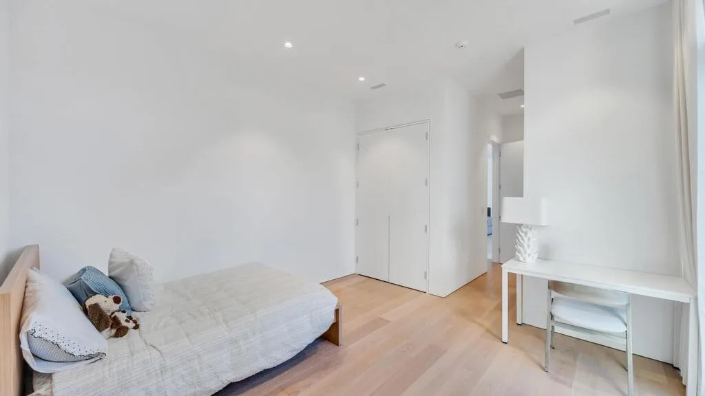 Una habitación luminosa y blanca con una cama baja y un escritorio pequeño.
