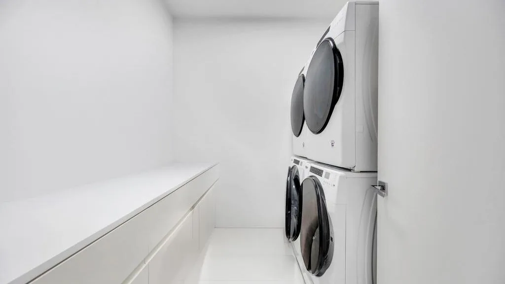 Un cuarto de lavandería con una lavadora y secadora apiladas junto a una encimera larga.