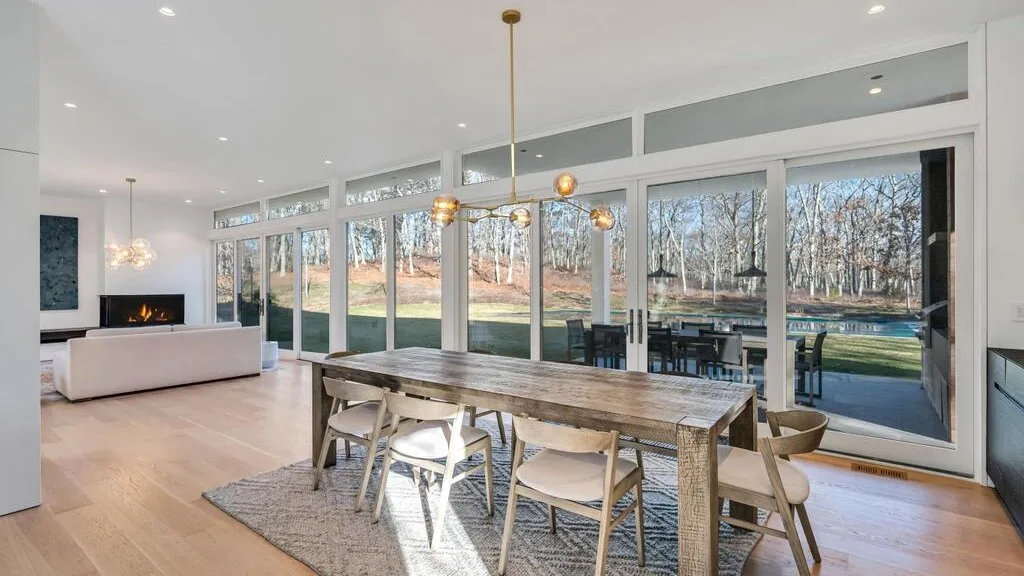 Un comedor luminoso con una mesa larga y grandes ventanales con vistas a un patio arbolado.