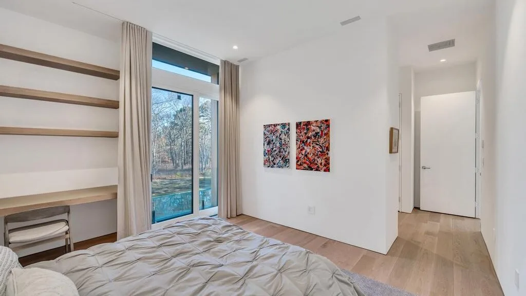Un dormitorio luminoso con una cama junto a una ventana grande y arte abstracto en la pared.