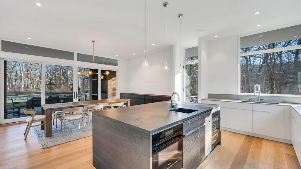 Una cocina y comedor diáfanos y luminosos, con una isla central y grandes ventanas.