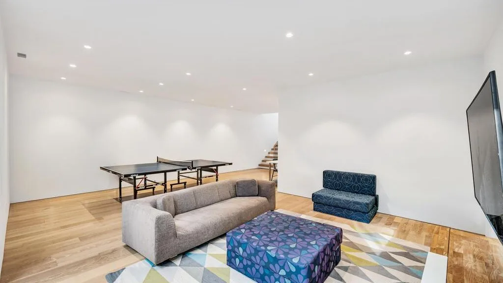 Una sala luminosa con un sofá, un otomano estampado y un pequeño sofá azul.