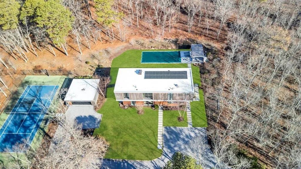 Una vista aérea muestra una casa moderna, césped, piscina y cancha de tenis.