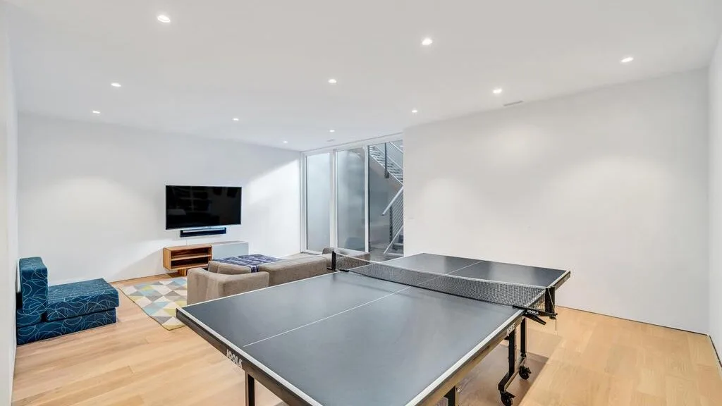 Una luminosa sala de recreación tiene una mesa de ping-pong, asientos y un televisor en la pared.