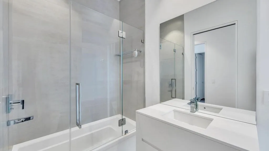 Un baño luminoso con ducha de vidrio y un tocador blanco.