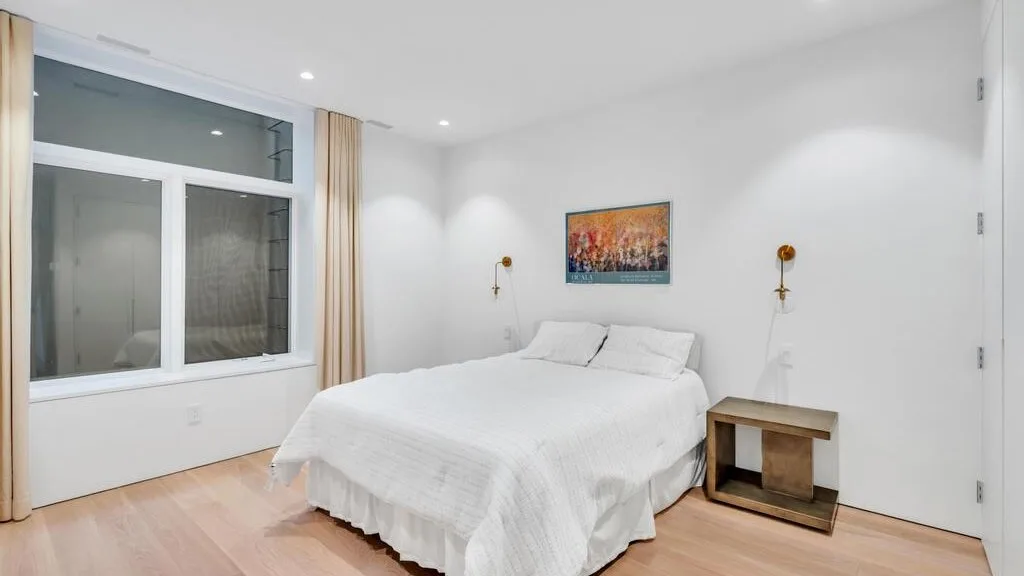 Un dormitorio luminoso con una cama bien tendida y una ventana grande.