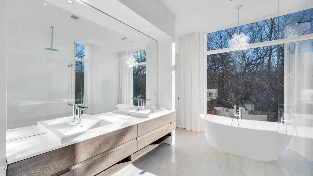 Un baño luminoso con lavabo doble y bañera exenta junto a grandes ventanas.