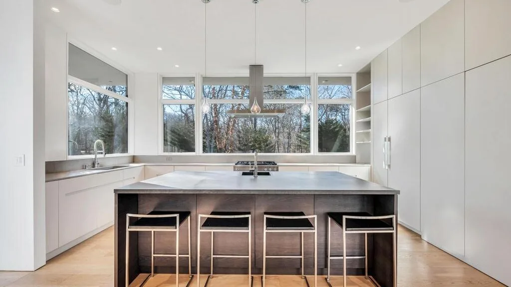 Una cocina moderna y luminosa con una gran isla y ventanas que dan a los árboles.