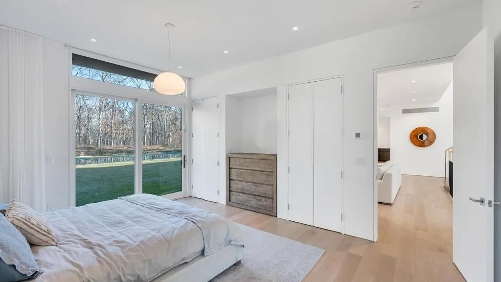 Un dormitorio luminoso con una cama junto a grandes ventanas que dan a un jardín.