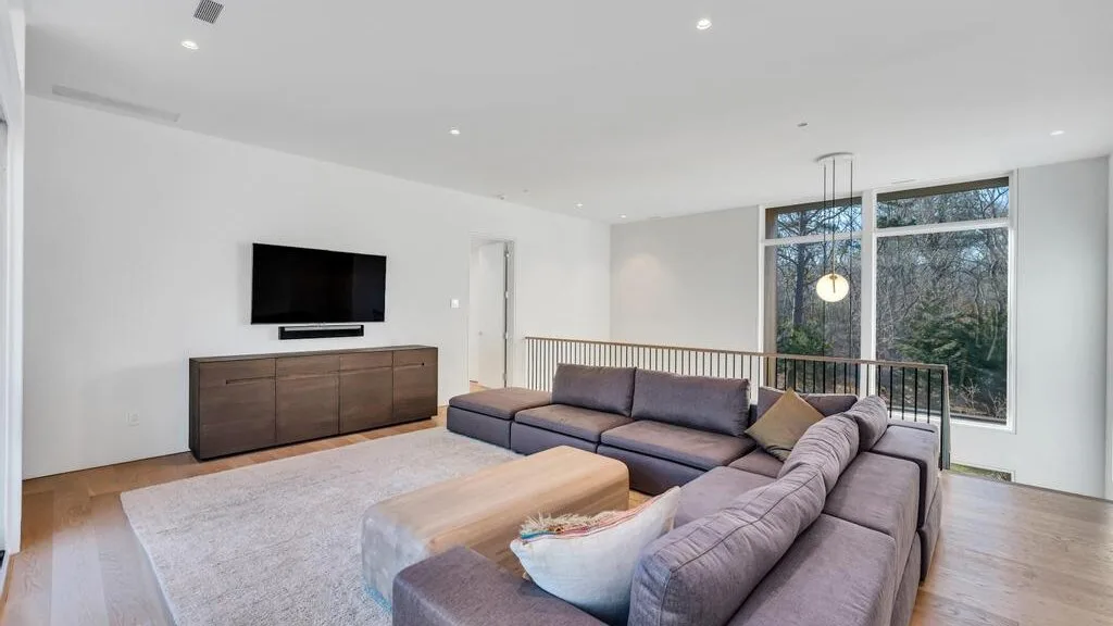 Una sala luminosa con asientos seccionales, televisor y grandes ventanas.