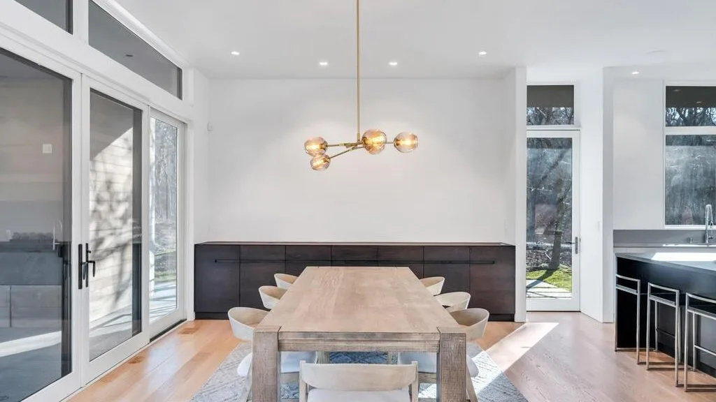 Una luminosa zona de comedor tiene una mesa larga bajo una lámpara colgante.
