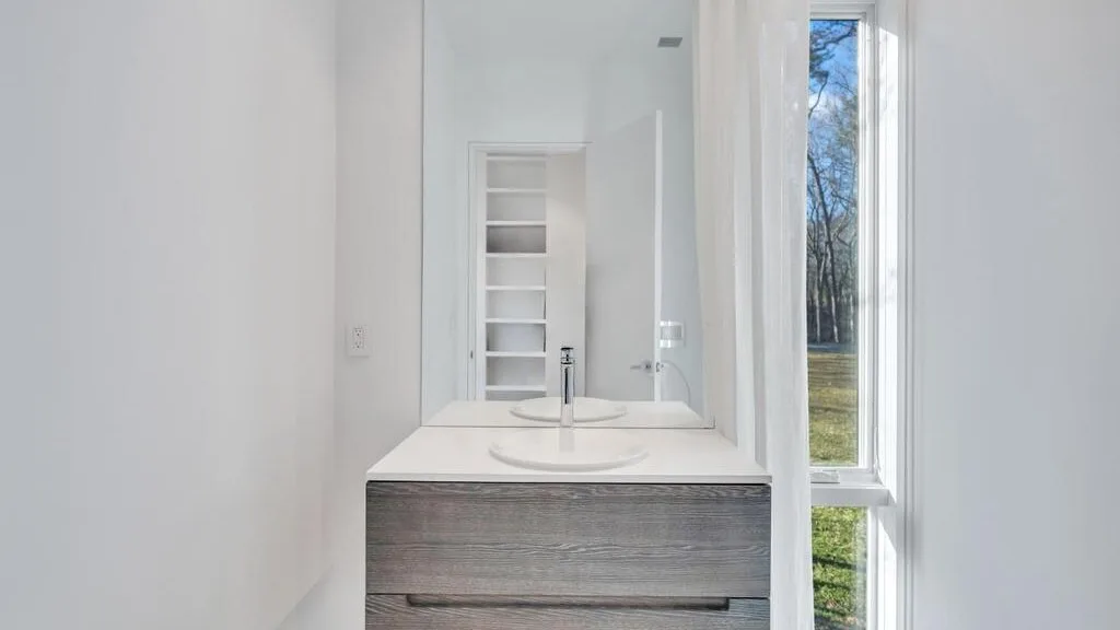 Un tocador de baño luminoso con lavabo junto a una ventana alta.