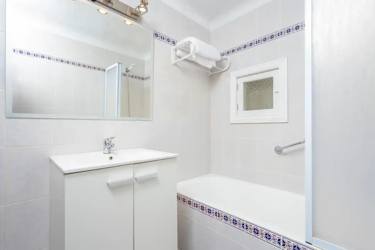 A bright bathroom with a sink, mirror, and bathtub.