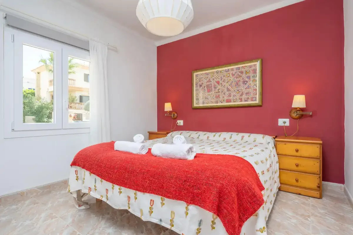 Bedroom with a bed covered by a red blanket and a window.