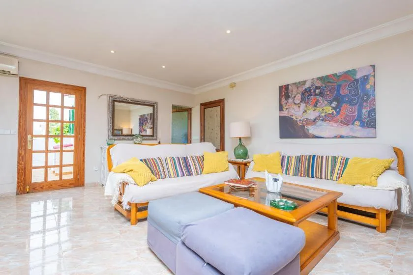 A bright living room with seating, a wooden coffee table, and colorful wall art.