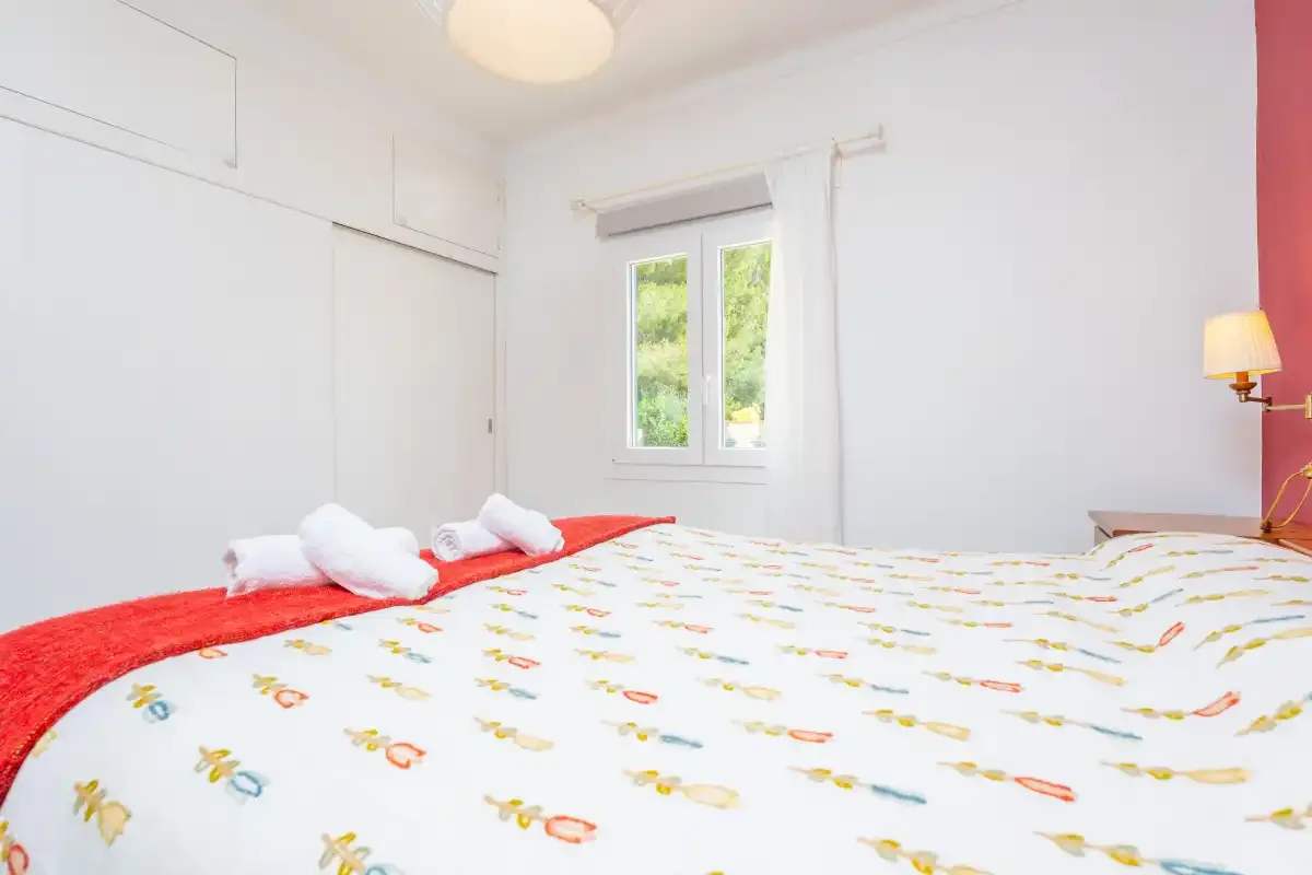 A bedroom with a patterned bedspread and a window overlooking greenery.
