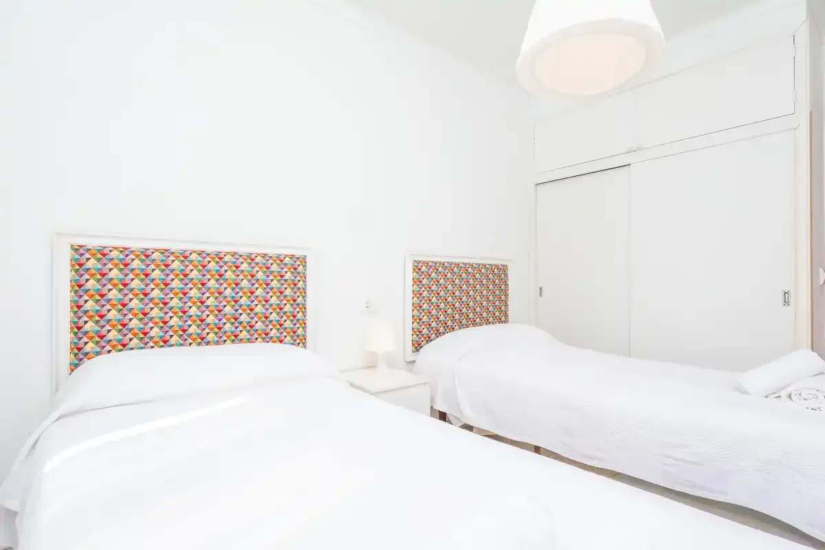 A bright bedroom with two beds featuring colorful patterned headboards.