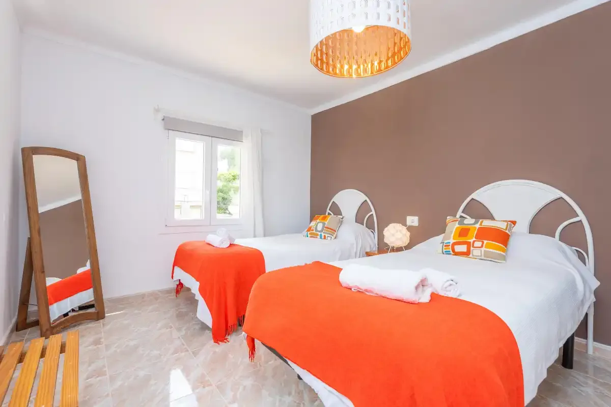 A bedroom with two beds dressed in white and bright orange bedding.