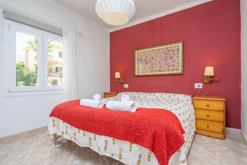 A bedroom with a bed dressed in red and white bedding beside a wooden dresser.