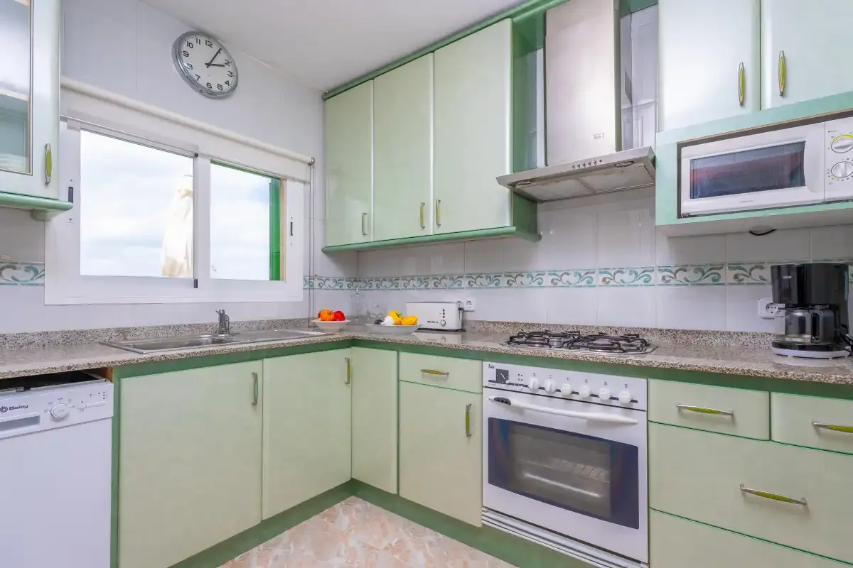 A bright kitchen with pale green cabinetry, a gas cooktop, and an oven.